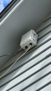 Closed weatherproof enclosure mounted on the siding under the eave with cables entering through cable glands